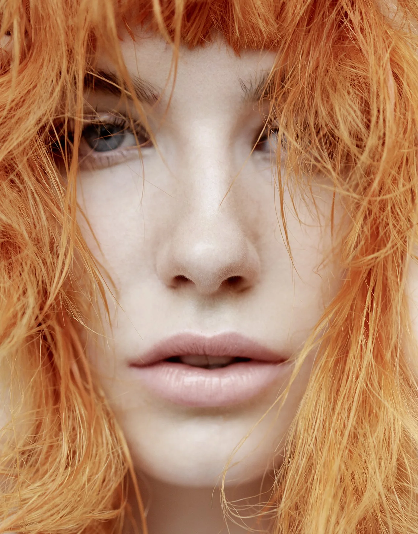 Nahaufnahme eines Gesichts mit roten, lockigen Haaren, blasser Haut und neutralem Ausdruck.