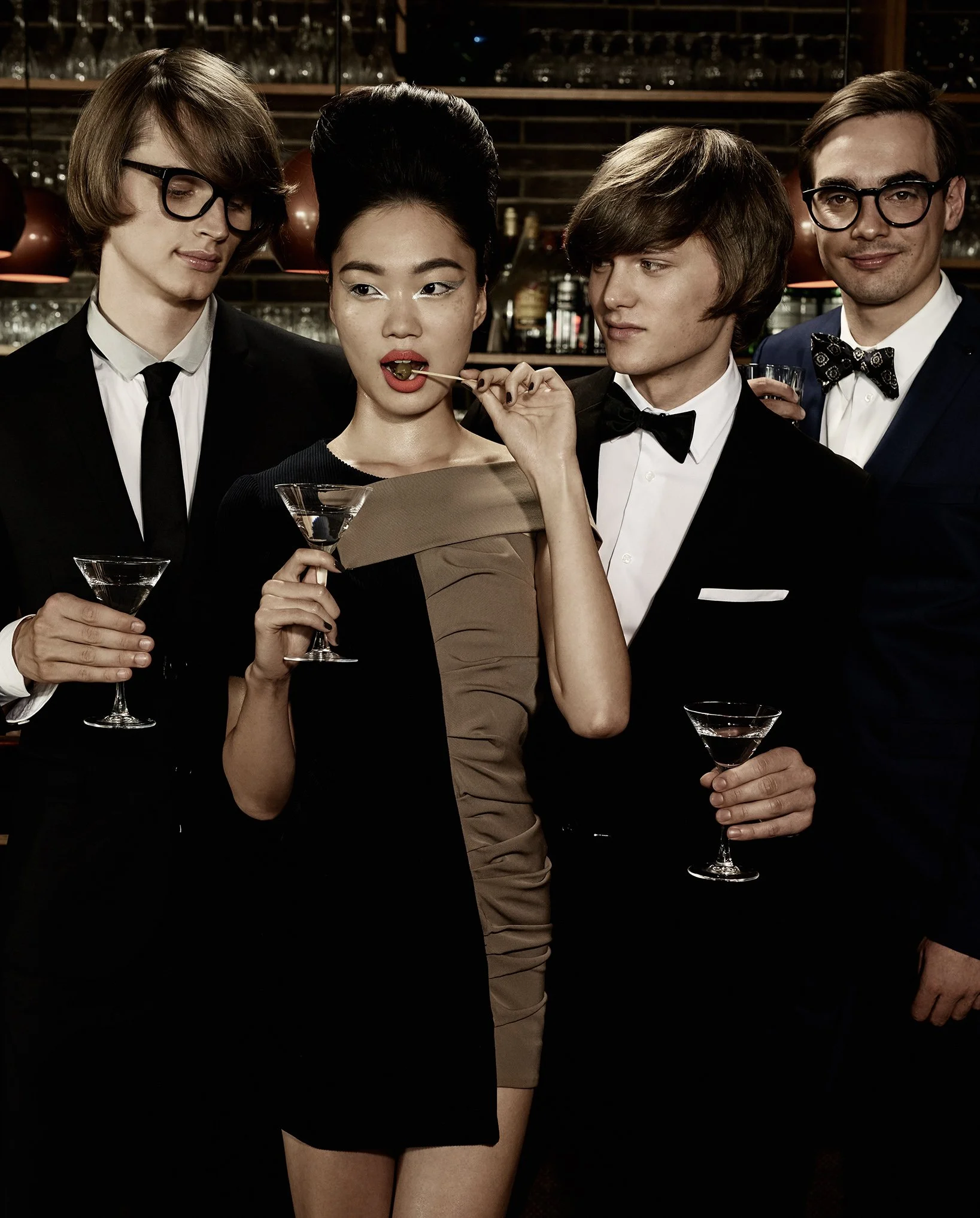 Eine Gruppe von vier Menschen in formeller Kleidung bei einer Party, mit der Frau in der Mitte, die einen Cocktail hält und an einem Cocktailstab kaut.