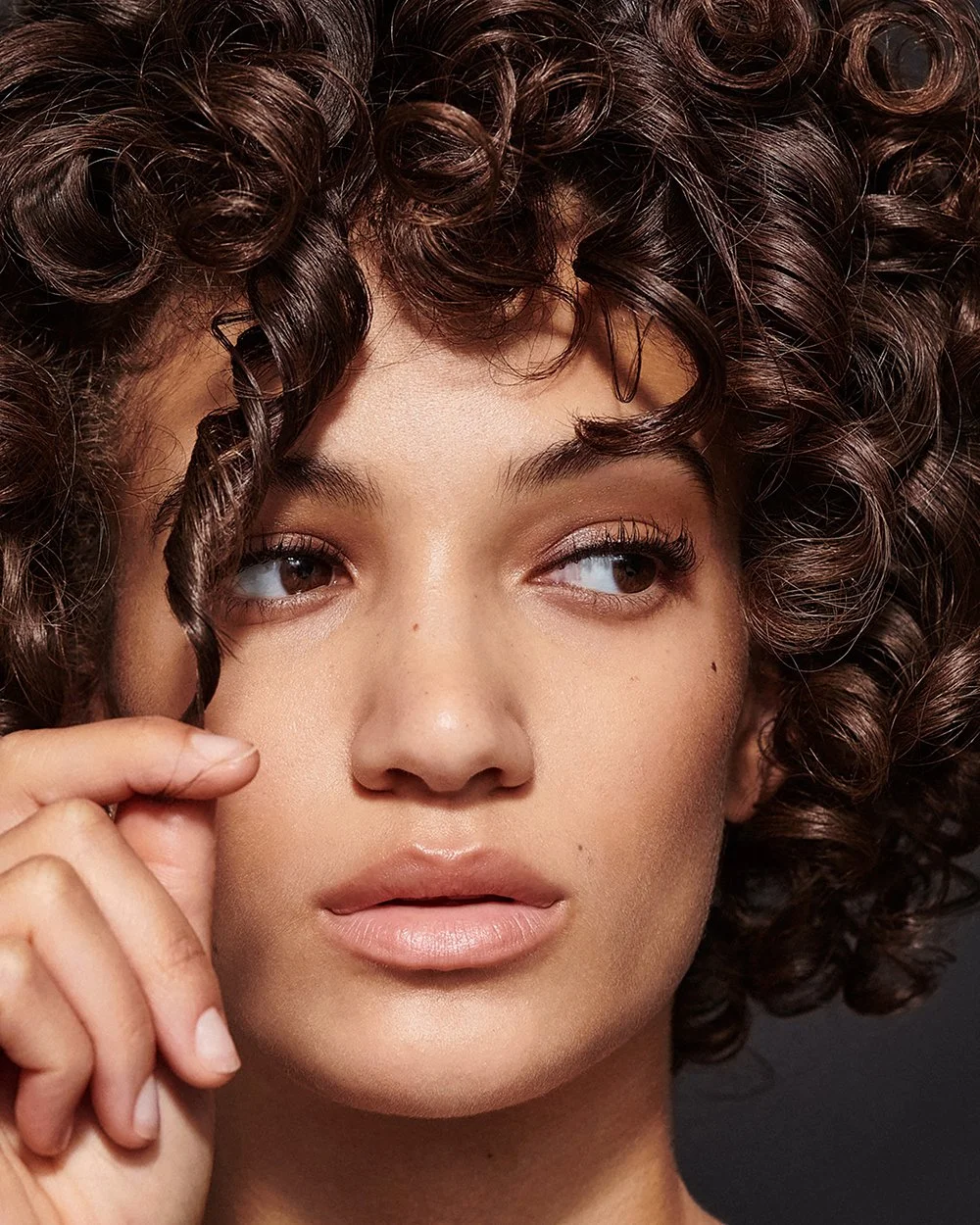 Nahaufnahme eines Mädchens mit dunklen, lockigen Haaren, das eine Hand in der Nähe des Gesichts hält.