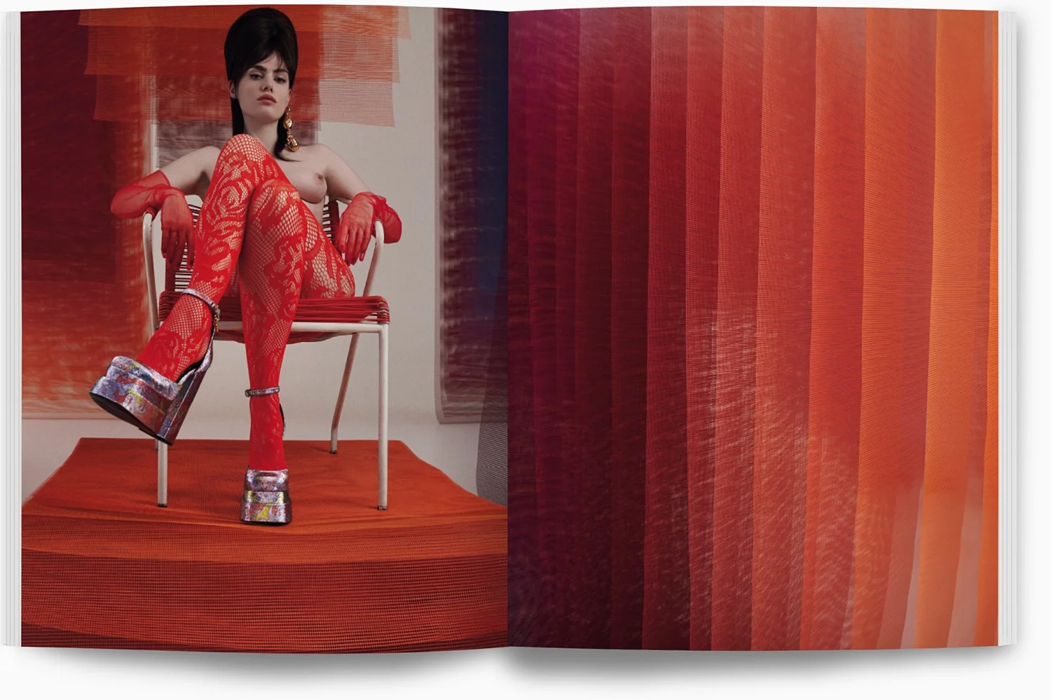 Eine Frau sitzt auf einem roten Stuhl, trägt rote Spitzenstrümpfe, rote Glove, auffällige Schuhe und hat kurze dunkle Haare, im Hintergrund sind verknotete, rote, verzerrte Vorhänge.