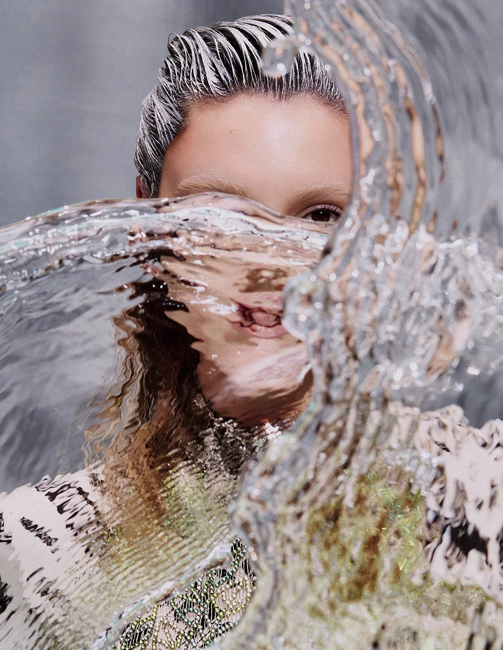Frau, die mit Wasser spielt und es aufnimmt, während sie auf einer Kamera sitzt, mit nassen Haaren und leichtem Lächeln.