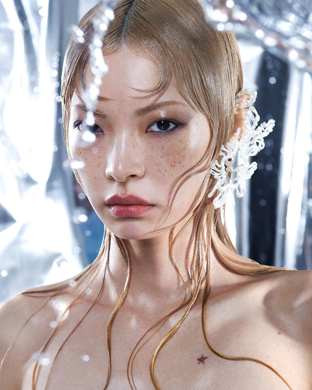 Nahaufnahme eines Mädchens mit feuchter, glatter Haut, roten Haaren, sichtbaren Sommersprossen, silbernem Make-up und dekorativen weißen, schneeförmigen Haaraccessoires.