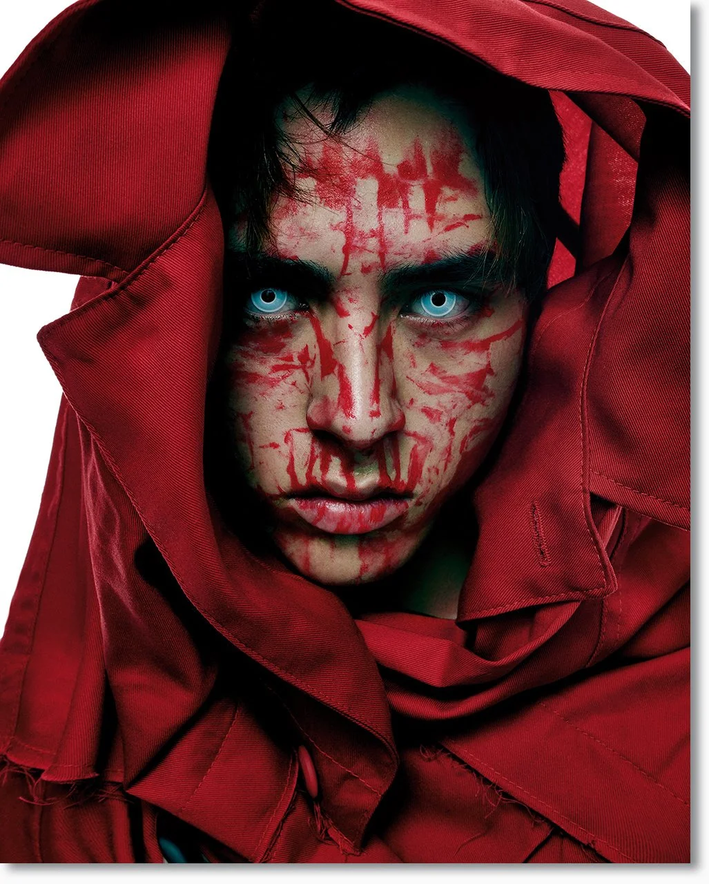 Nahaufnahme eines Mannes mit blauen Augen, roter Kleidung und roten Mustern im Gesicht, die wie Blut wirken, mit einem ernsthaften Blick direkt in die Kamera.