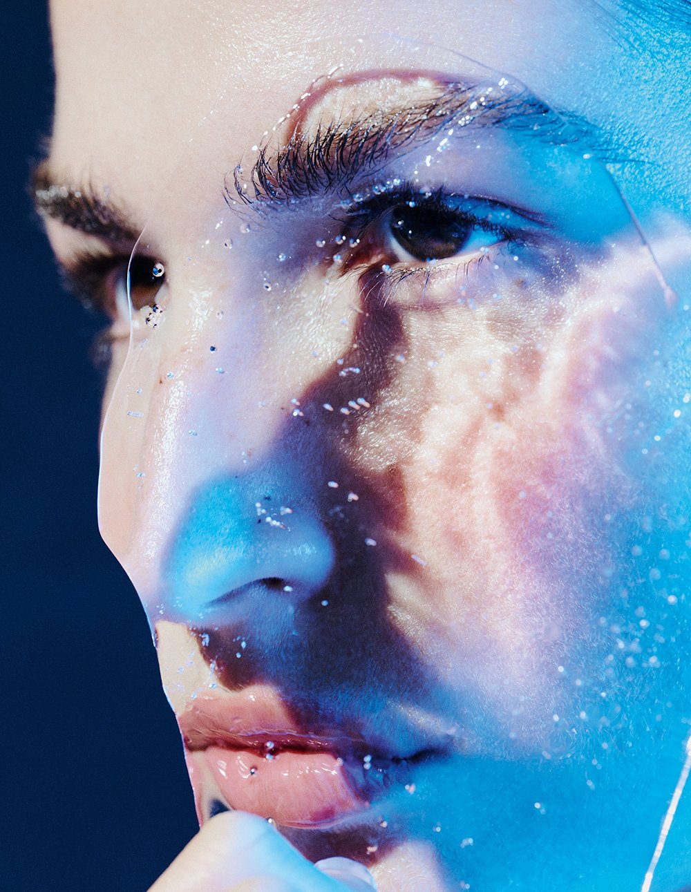 Nahaufnahme eines menschlichen Gesichts mit feuchten Haut, sichtbaren Poren und Gesichtshaare, das von blauer und rosa Beleuchtung beleuchtet wird.