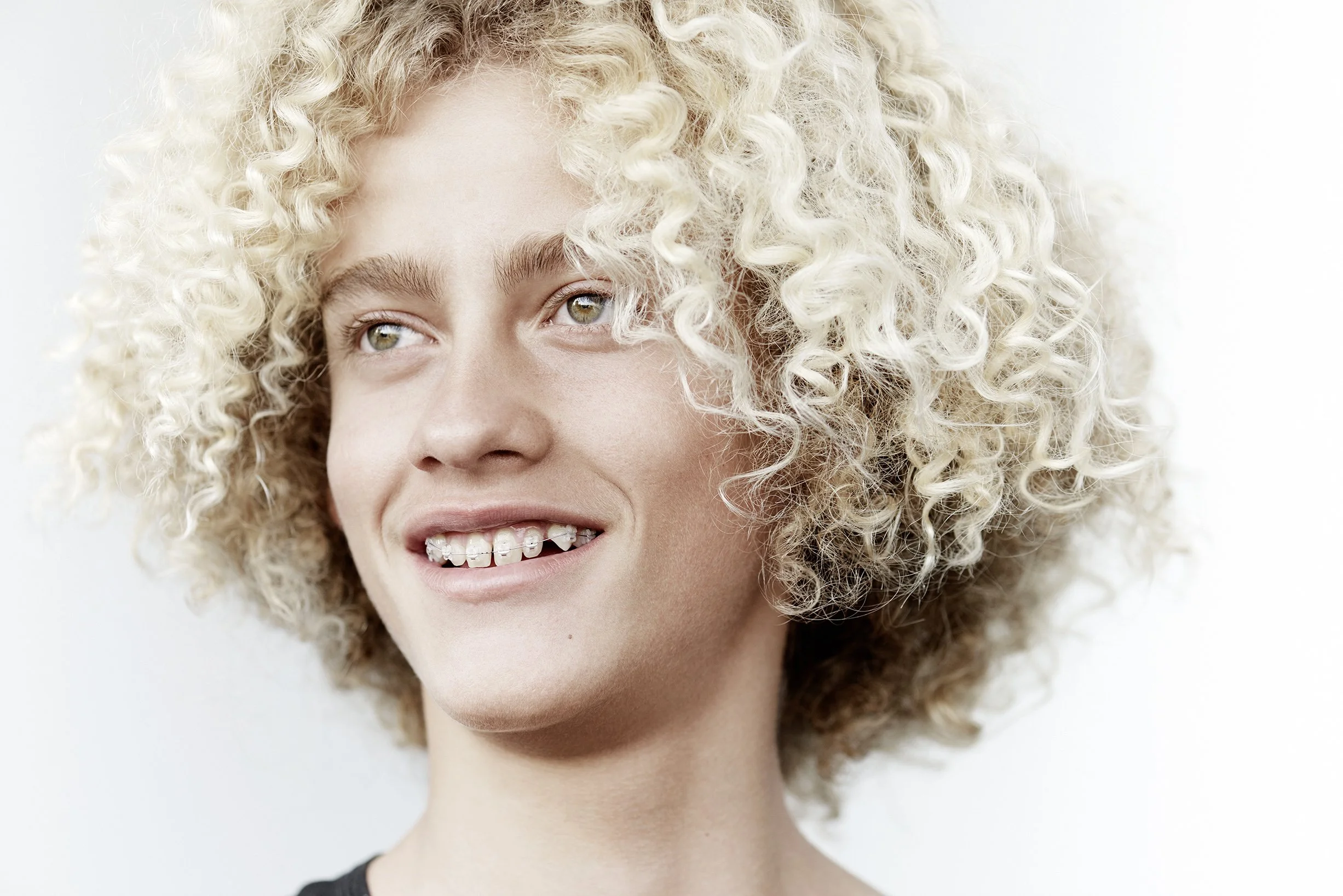 Lächelnde Frau mit blonden lockigen Haaren, sichtbare Zahnspange