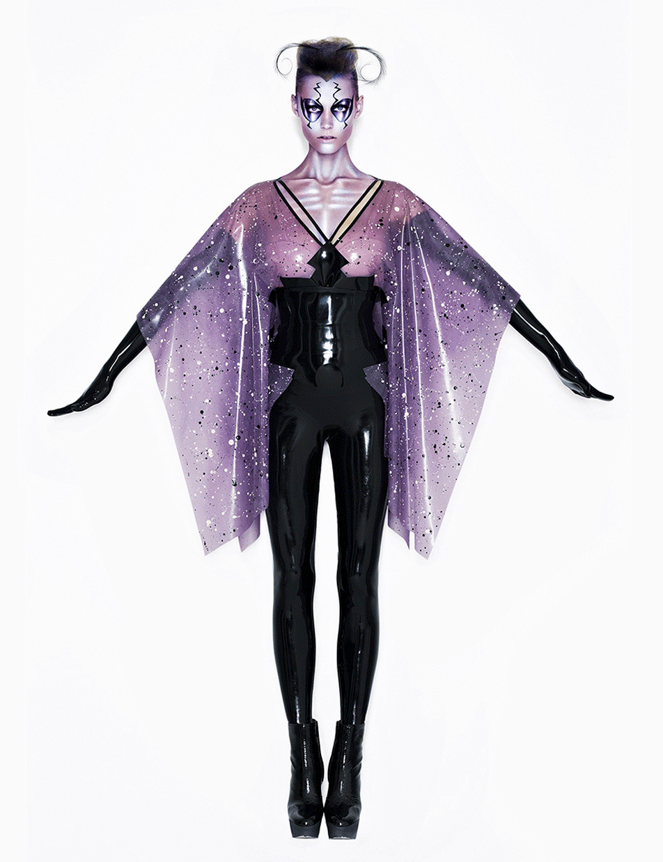 Modell in futuristischem schwarzen Latex-Outfit mit lilafarbenem, schimmerndem Cape, Make-up im Stil eines Schattens, stehend vor weißem Hintergrund.
