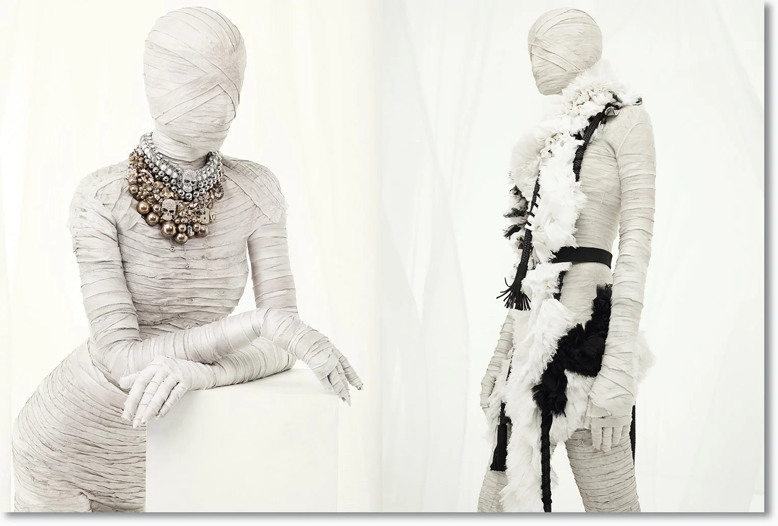 Kunstinstallation mit zwei Skulpturen, die vollständig in Weiß gekleidet sind, eine trägt große Perlenketten und die andere eine schwarze und weiße gestreifte Deko.