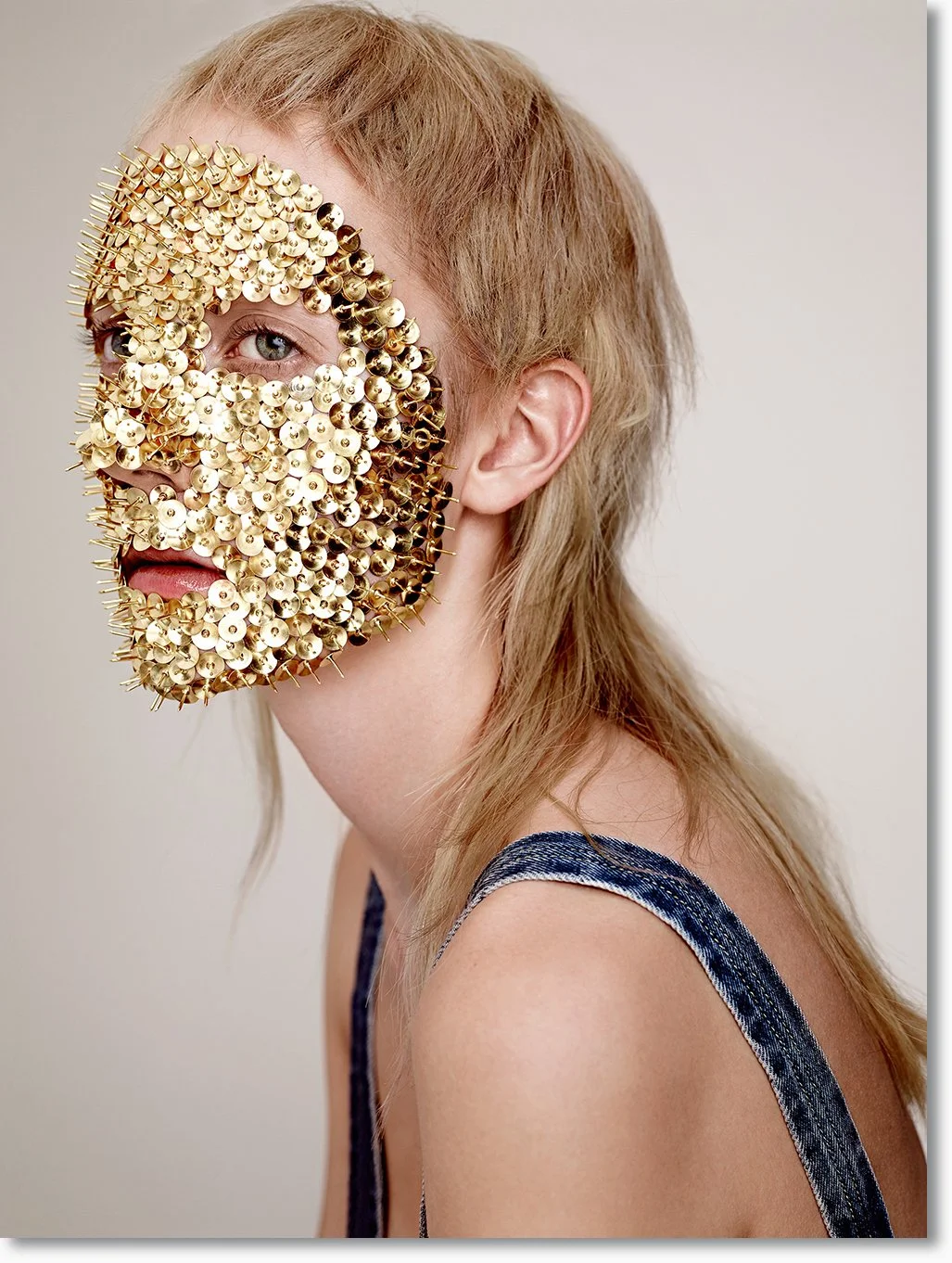 Person mit einem total bedeckenden goldenen, stacheligen Masken, die nur ein Auge und den Mund sichtbar lässt.