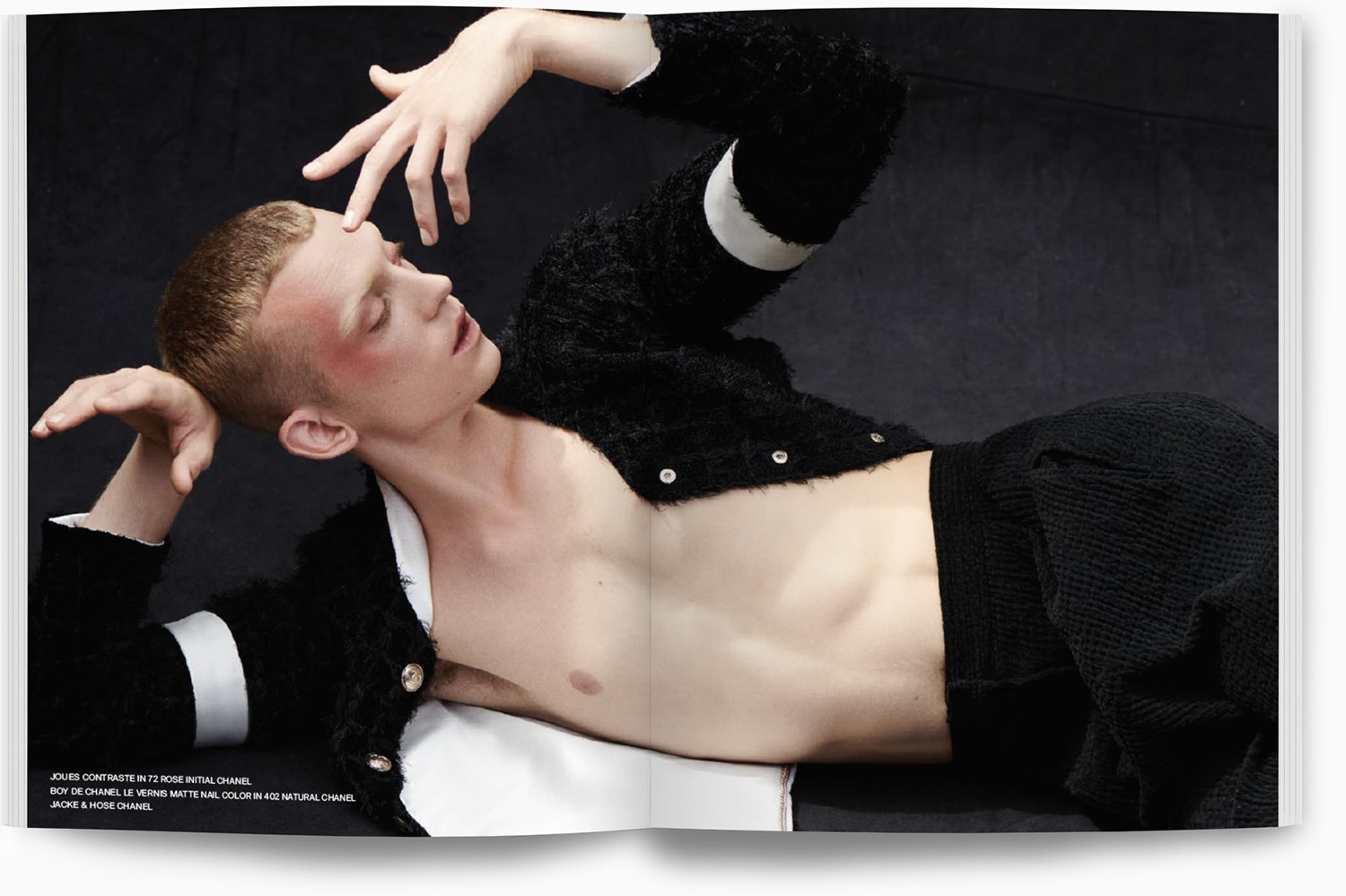 Junge liegt auf dem Boden, trägt schwarze Jacke und Hose, ist nackt bis auf die Jacke, mit geschlossenen Augen, entspannt, schwarze Hintergrund.