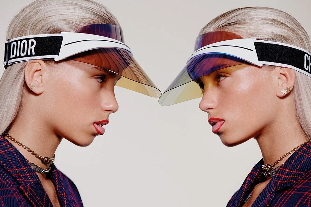 Zwei Frauen mit silbernem Haar tragen Dior-Vizinstrumente und bunte Sonnenblenden, die sich berühren.