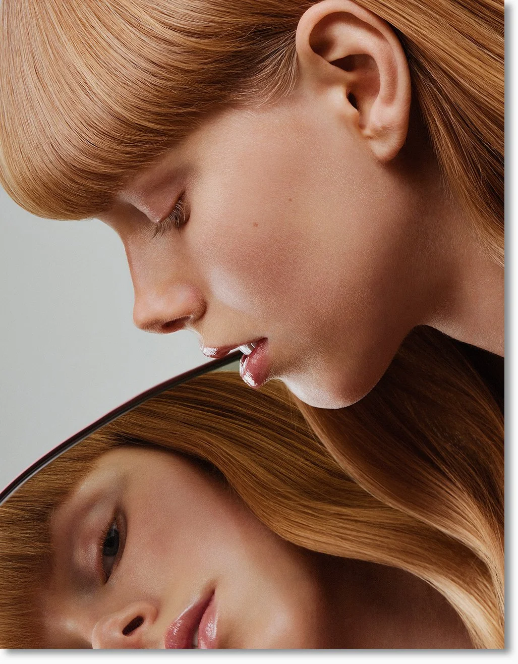 Nahaufnahme eines mädchenhaften Gesichts mit roten, glänzenden Haaren, das in eine runde Spiegel blickt.