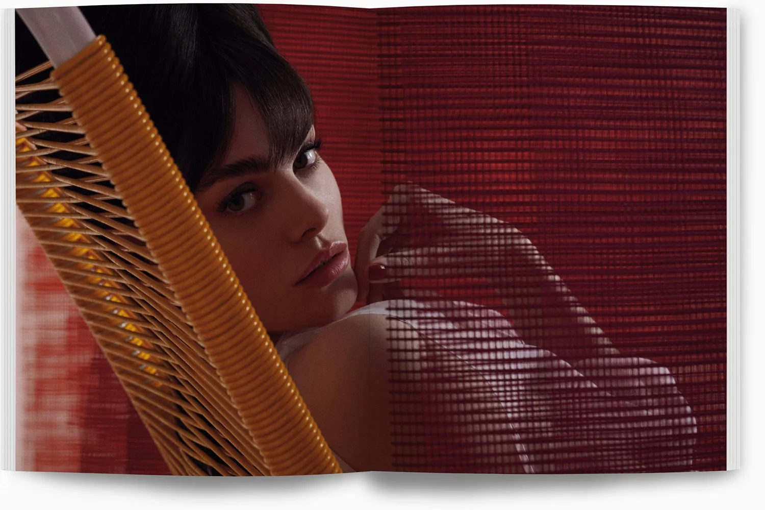 Nahaufnahme eines jungen Mädchens mit dunklen Haaren, das sich hinter einem roten Bambusrollo befindet, nur ihr Gesicht und ihre Schulter sind sichtbar.