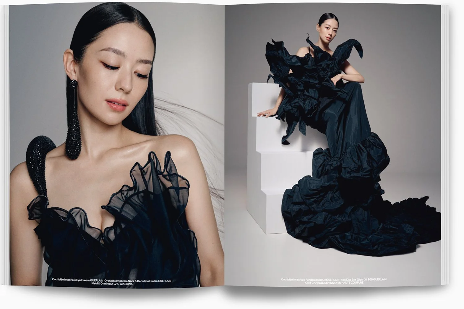 Zweiteiliger Modekatalog mit einer asiatischen Frau in einem schwarzen, rüschigen Kleid und einer großen schwarzen Schulterkette. Sie sitzt auf weißen Blöcken gegen einen grauen Hintergrund.