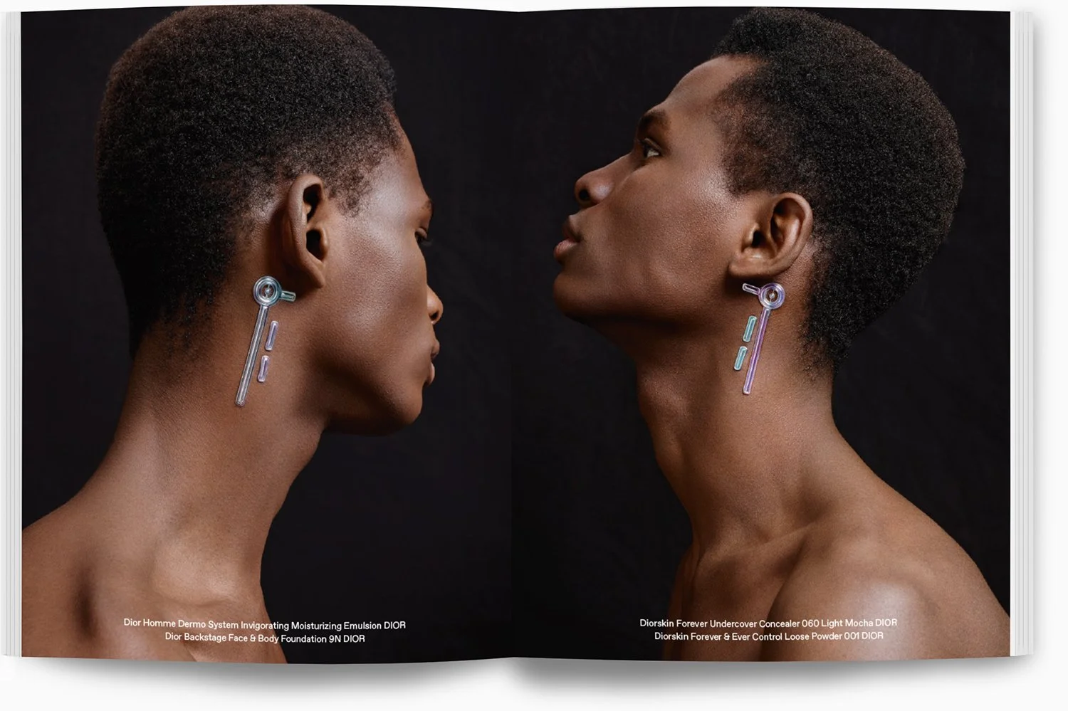 Zwei dunkelhäutige Frauen mit kurzen Afro-Haarschnitten tragen moderne, transparente Ohrringe gegen einen schwarzen Hintergrund. Die Frauen sind sich gegenübersitzend, die Köpfe fast berührend, mit ausdrucksvollen Gesichtsausdrücken.