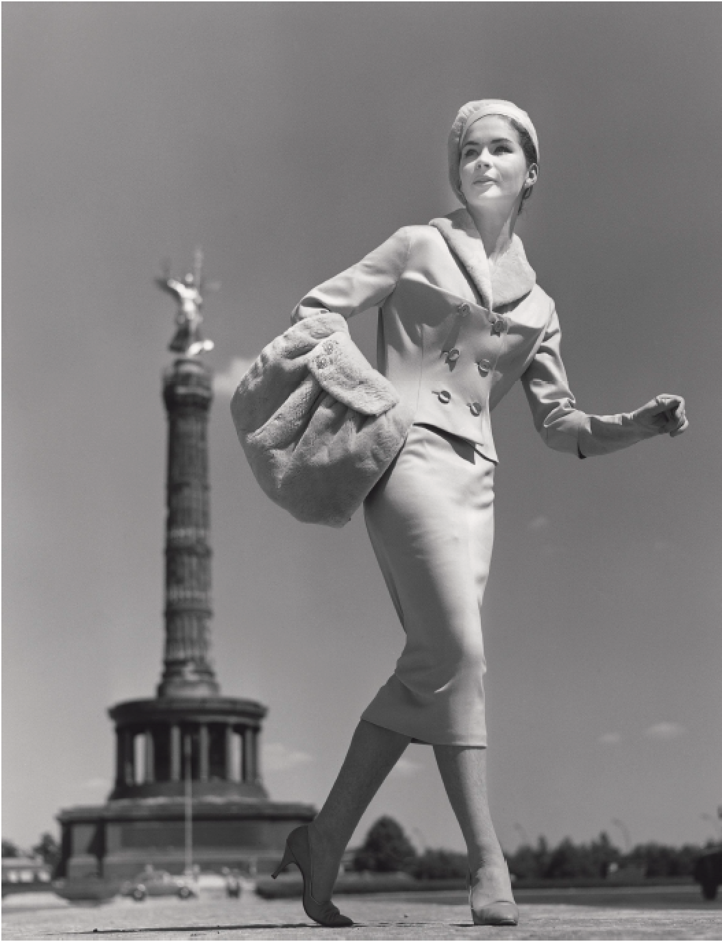 Eine schwarz-weiß Aufnahme einer stilisierten Dame in eleganter Kleidung, die eine Tasche trägt, vor dem Berliner Siegessäule im Hintergrund.