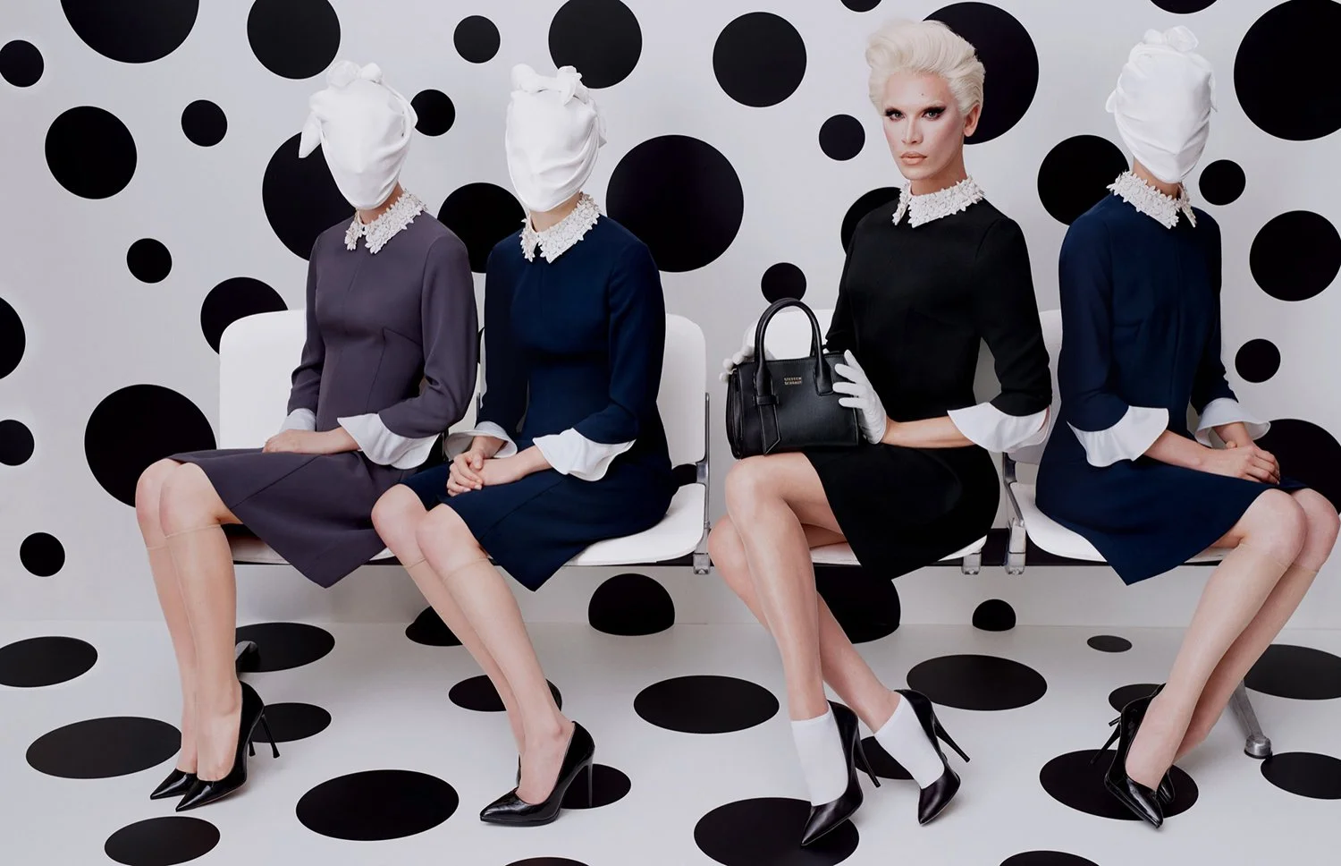 Four women with platinum blonde hair sitting on a white bench against a black and white polka dot background. They are dressed in elegant, vintage-style dresses with white cuffs and collars, wearing black high heels. The second woman is holding a bla