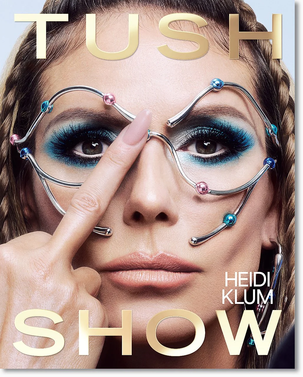 Cover eines Magazins mit einem Porträt einer Frau mit auffälligem blauen Make-up, großen Brillengläsern, die mit bunten Perlen verziert sind, und der Aufschrift ‚TUSH SHOW‘ sowie dem Autorennamen ‚Heidi Klum‘.