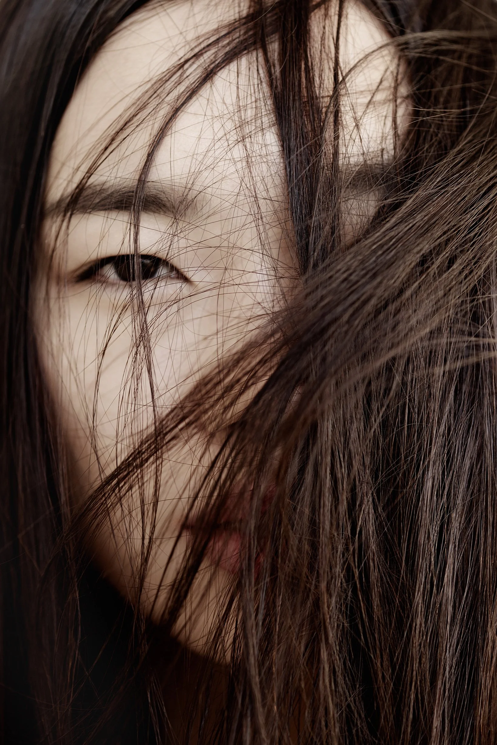 Nahaufnahme eines Gesichts mit langen braunen Haaren, die das Gesicht teilweise bedecken, und einem Auge, das halb sichtbar ist.