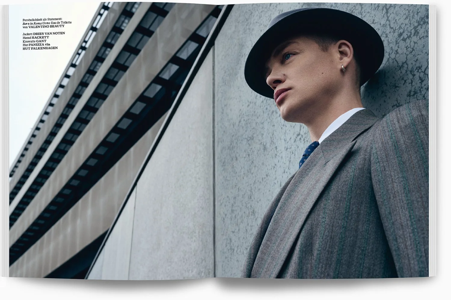 Junge Frau in Anzug und Hut lehnt an einer Betonwand vor einem modernen Hochhaus