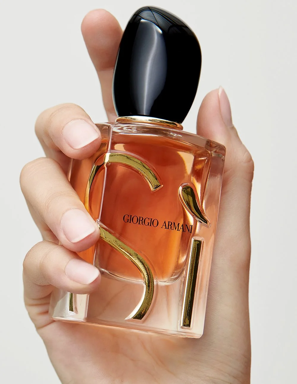 Hand hält eine Flasche Giorgio Armani Sì Eau de Parfum mit gestalterischem goldfarbenem SEL-Logo.