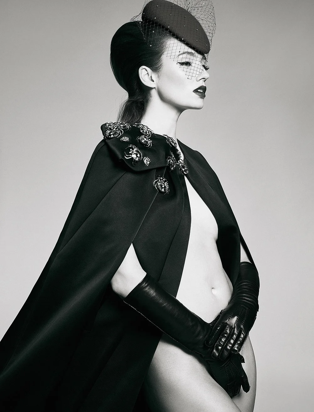 Schwarz-weiß-Fotografie einer stilvollen Frau mit aufwendig gestyltem Haar, Kerchief und Handschuhen, in einem eleganten, fashionbewussten Look.