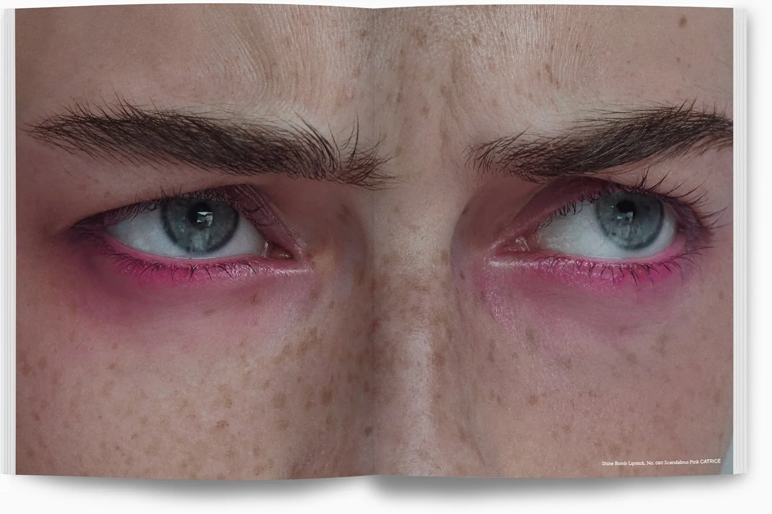 Nahaufnahme von blauen Augen mit rotem Eyeliner und braunen Augenbrauen, feine Haut mit Sommersprossen. Es handelt sich um ein aufgemaltes Bild, vermutlich in einem Magazin.