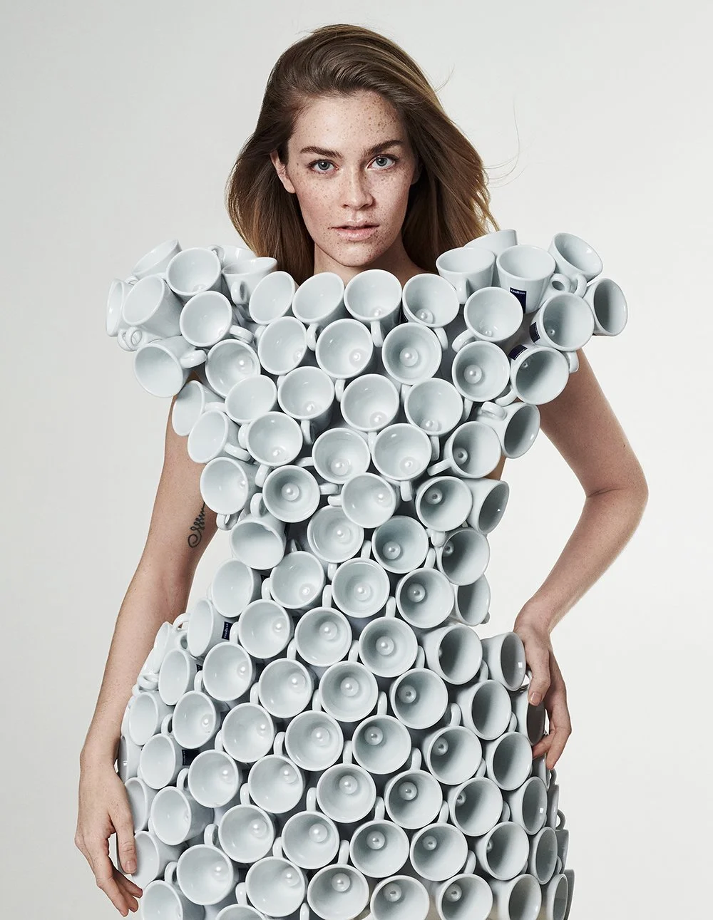 Frau trägt Kleid aus weißen Keramik- oder Porzellan-Tassen.