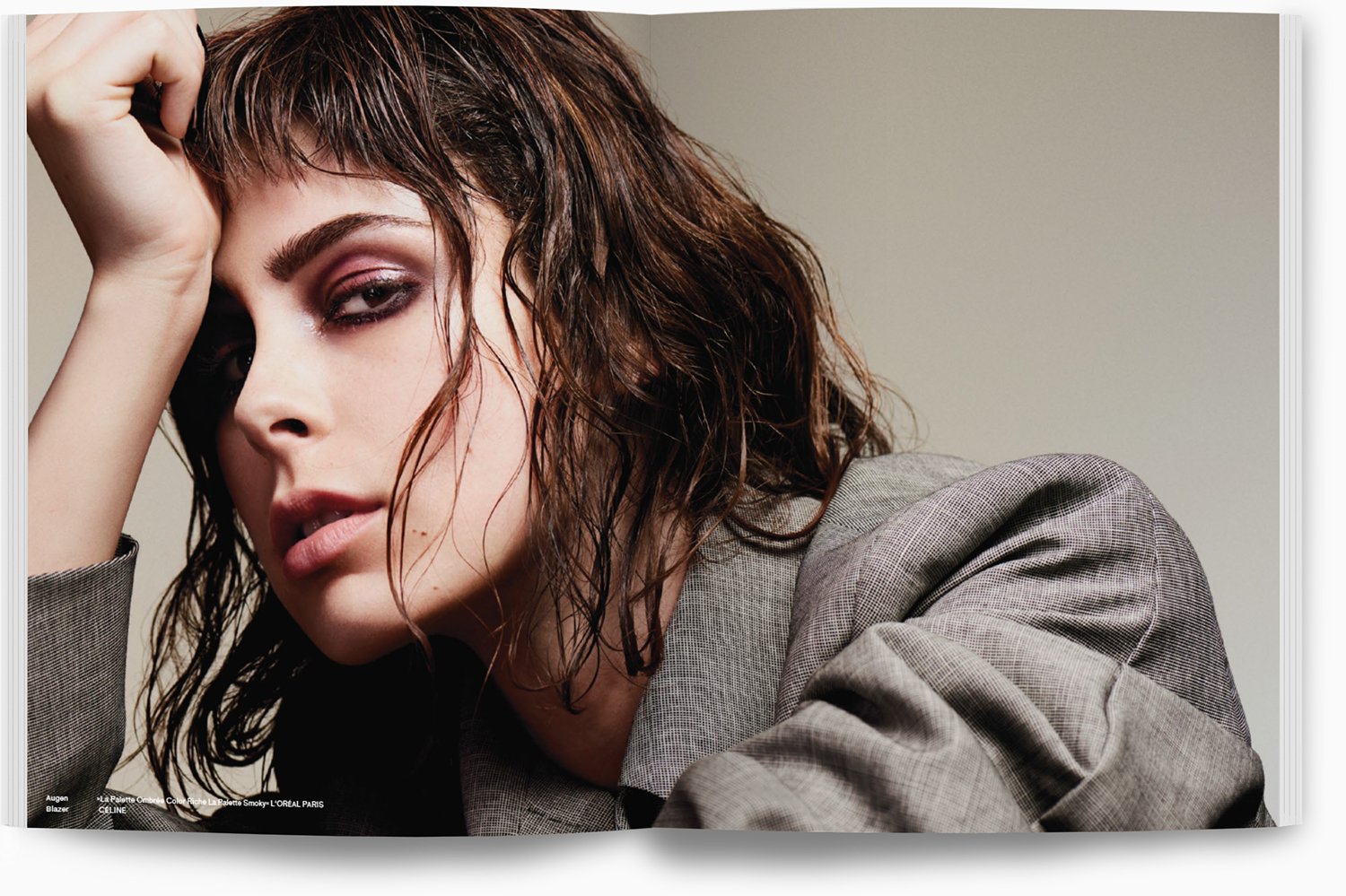 Nahaufnahme eines modischen Models mit nassen, lockigen braunen Haaren und Make-up, trägt einen grauen Blazer.