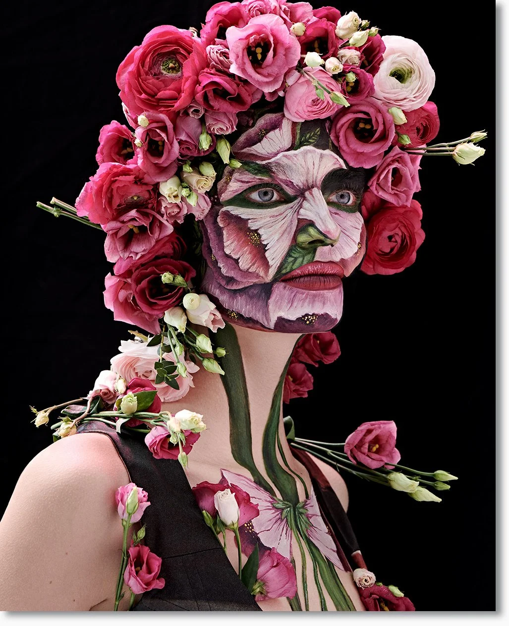 Eine weibliche Person mit Gesichtsmalerei, die Blumen in Pink, Rot und Weiß trägt, die das Haar, das Gesicht und den Körper bedecken, vor einem schwarzen Hintergrund.