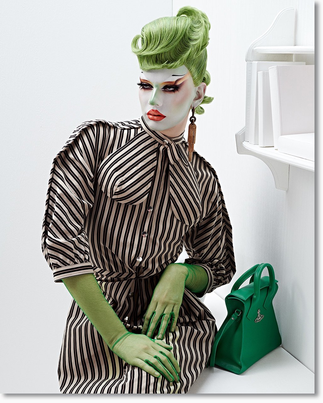 Modisch geschminkte Person mit grüner Frisur, gestreiftem Kleid, grünen Handschuhen und grüner Tasche in weißem Raum.