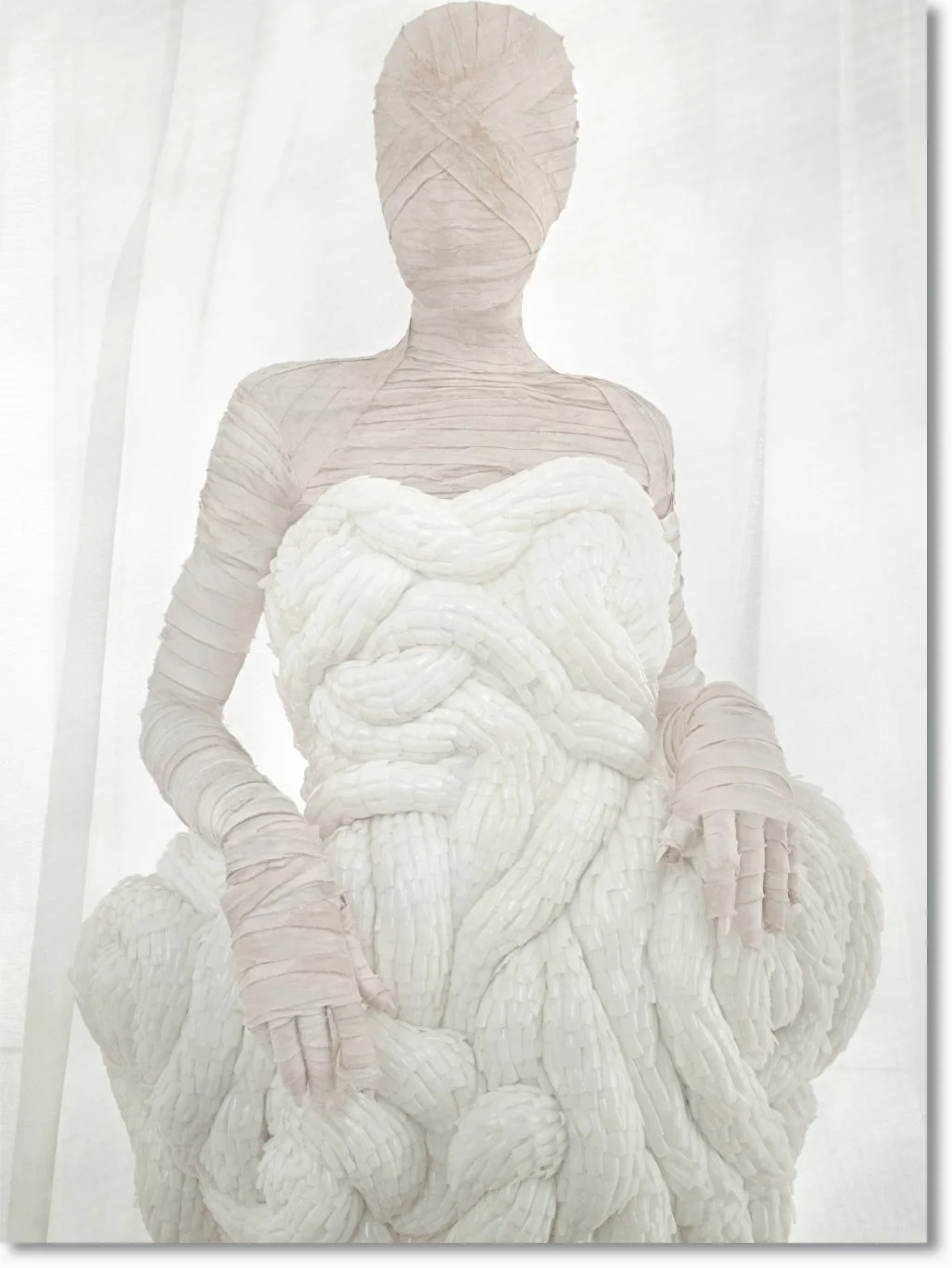 Skulptur einer sitzenden weiblichen Figur, die aus Papierkreisen besteht, mit einem Bauch, der Windungen und Schleifen ähnelt.