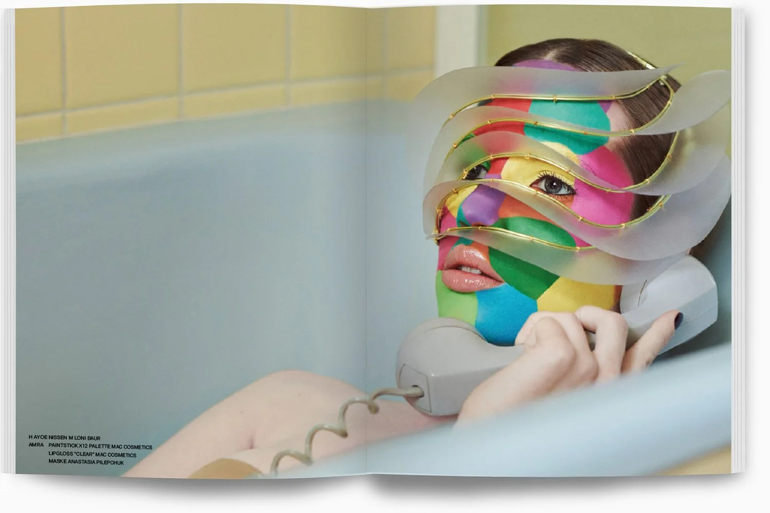 Frau im Wasser mit buntem Gesichtsmalerei, verschlungene transparente Spiralfolie vor dem Gesicht, im Wasser sitzend, mit Wasserhahn in der Hand.