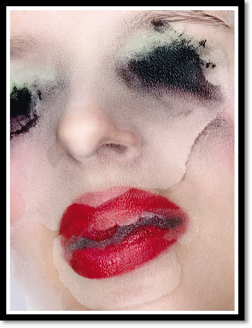 Nahaufnahme eines Gesichts mit geschminkten roten Lippen, schwarze Augen-Make-up und blasse Haut, durch einen transparenten Schleier oder Stoff leicht verzerrt.