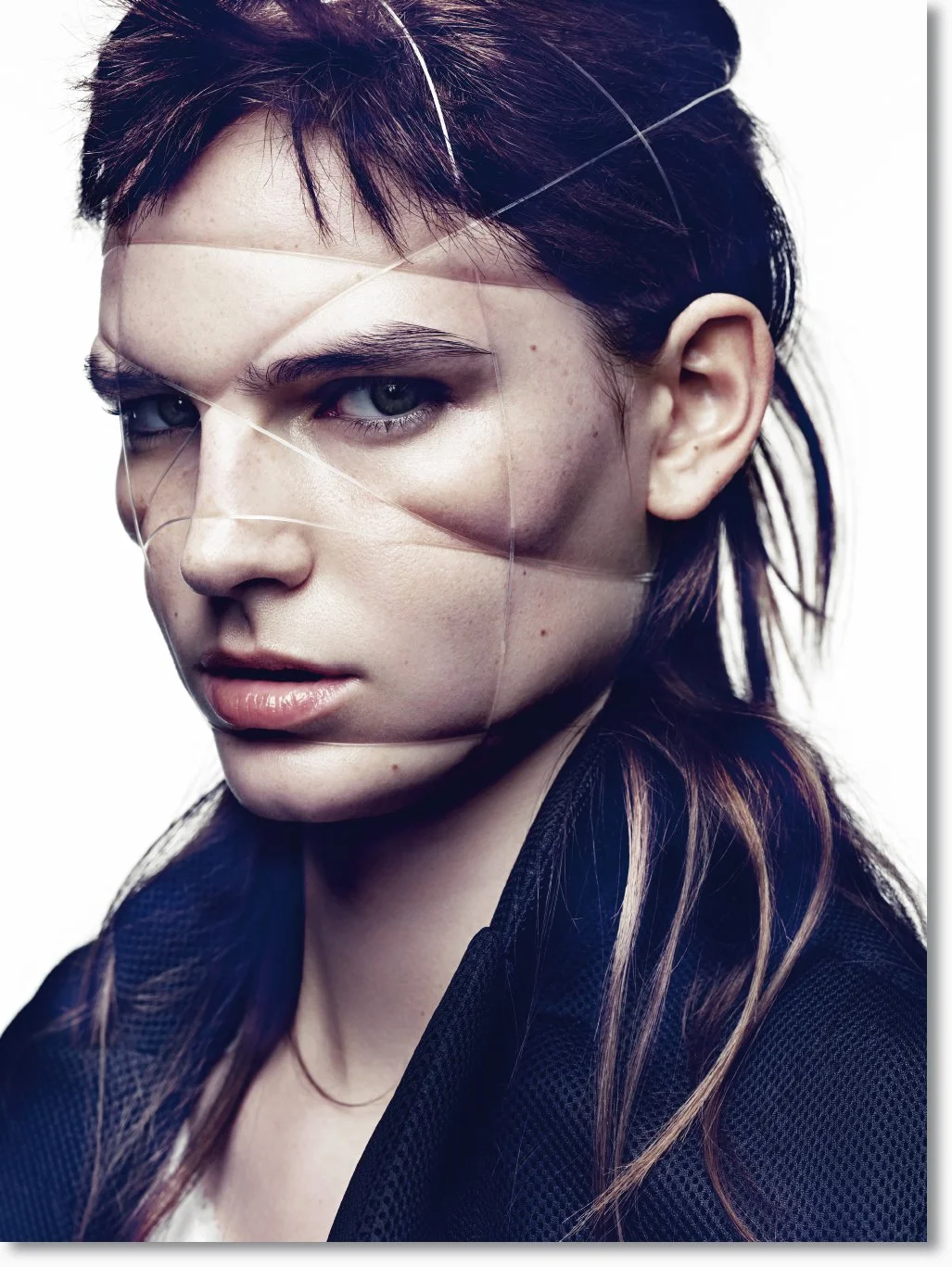Ein junges Mädchen mit dunklem Haar und blauen Augen, das eine beeindruckende, künstlerische Gesichtsmaske trägt, die aus dünnen, weißen Fäden besteht.