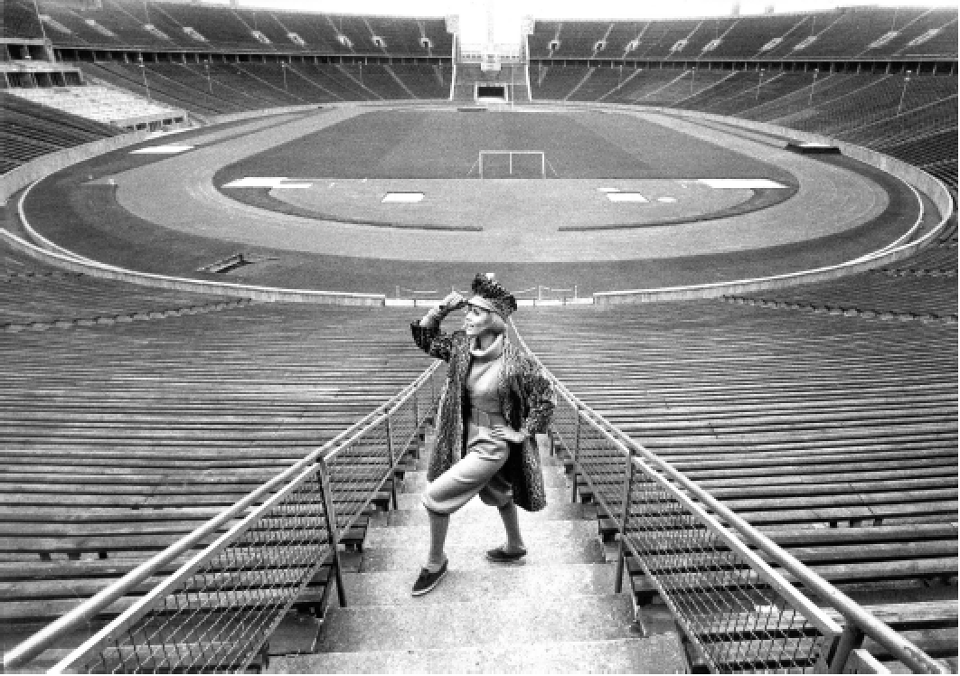 Leeres Stadion mit einer sitzenden Person in der Mitte, die auf die Kamera blickt, in Schwarz-Weiß.