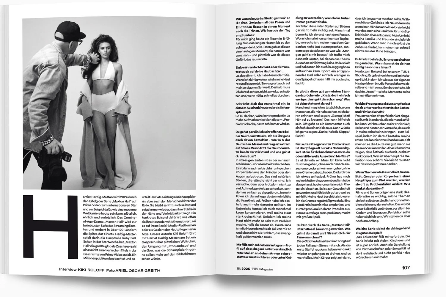 Ein Fotoshooting-Set mit einer jungen Frau in weißem Bikini und langen weißen Mantel, die vor einem grauen Hintergrund steht. Ein Mann neben ihr fotografiert sie. Der Raum ist hell, der Boden grau.