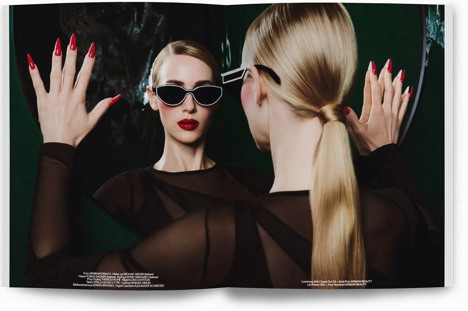 Zwei Frauen spiegeln sich in einem schwarzen, glänzenden Spiegel. Eine trägt schwarze Sonnenbrille und rote Lippen, die andere hat lange blonde Haare in einem Pferdeschwanz. Beide haben lange rote Nägel und tragen schwarze transparenten Kleidung.