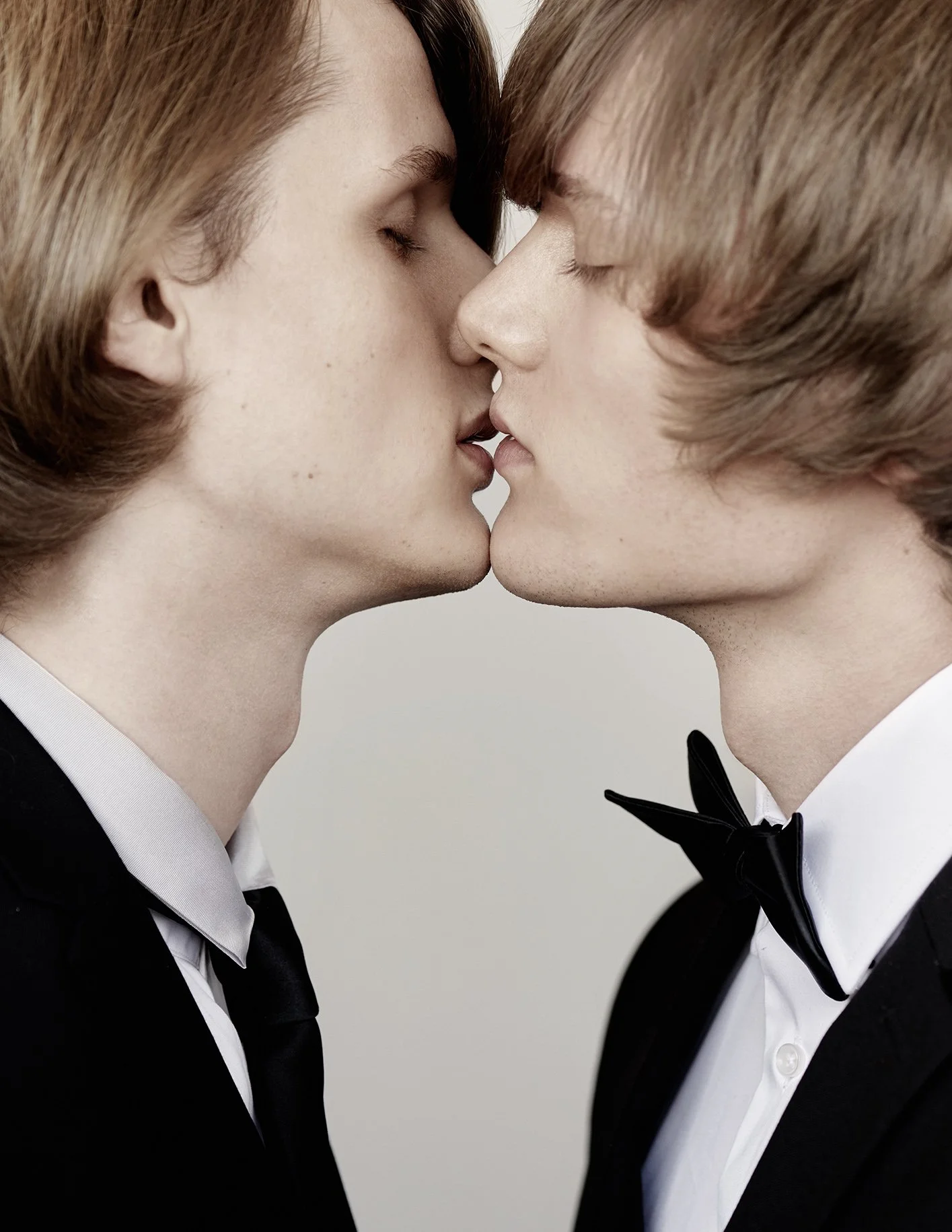 Zwei Männer in formeller Kleidung, die sich fast küssen, mit ihren Gesichtern nah beieinander und geschlossenen Augen.
