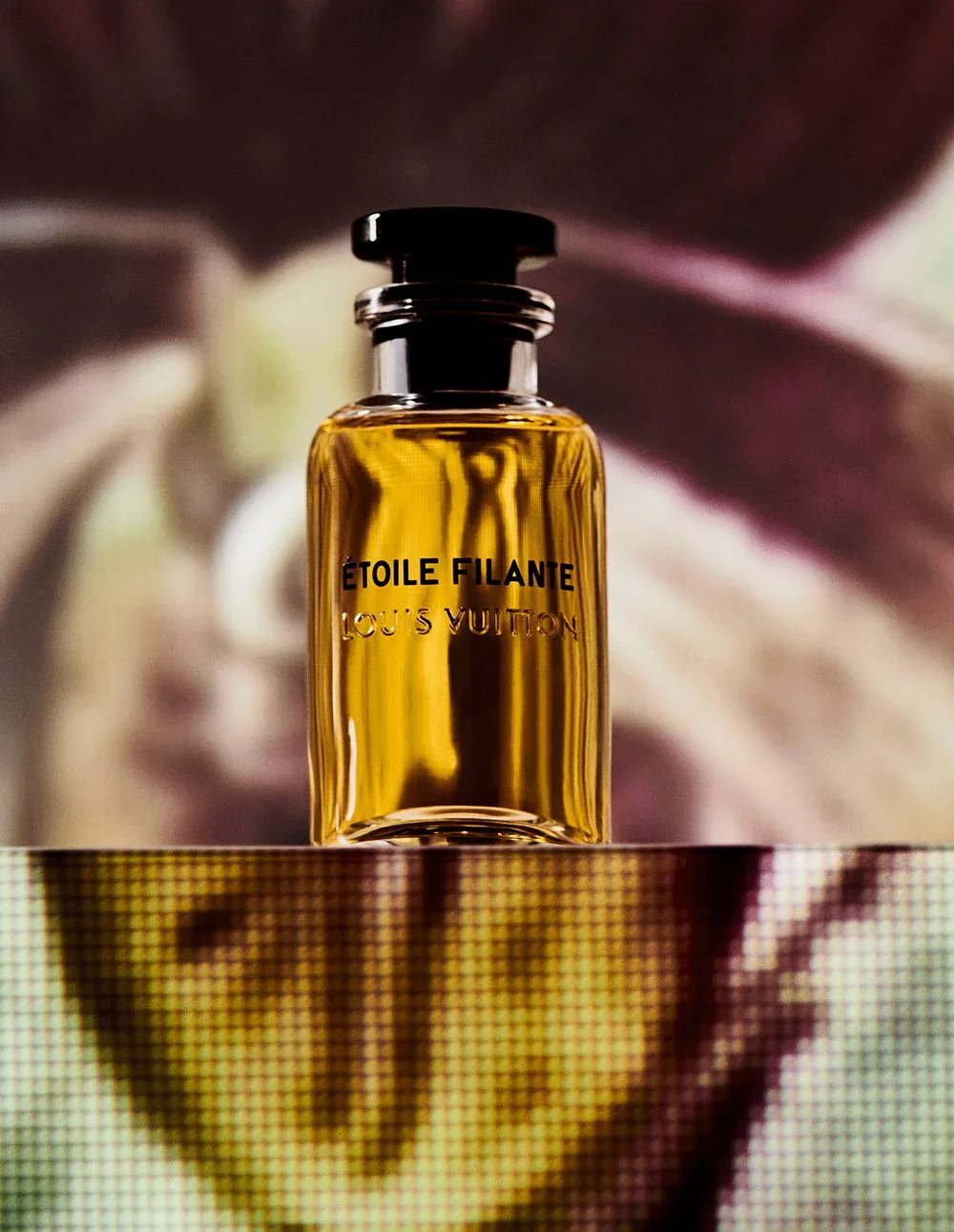 A bottle of Louis Vuitton Etoile Filante perfume standing on a reflective surface with a blurred abstract background.