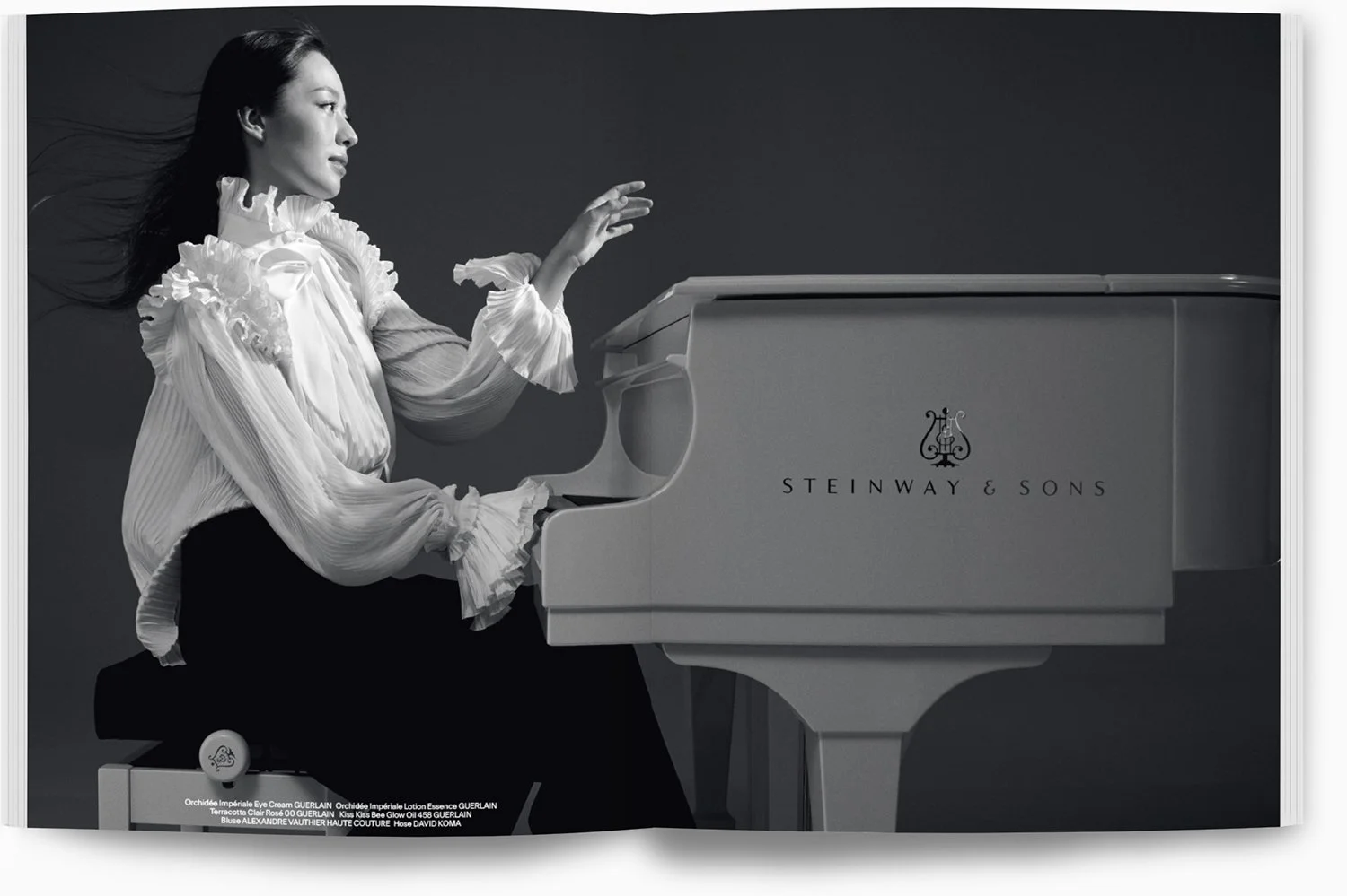 Schwarz-weiß Bild einer Frau, die an einem weißen Steinway & Sons Klavier spielt, mit einer eleganten weißen Bluse und langen Haaren, im Hintergrund ein dunkler, einfacher Hintergrund.
