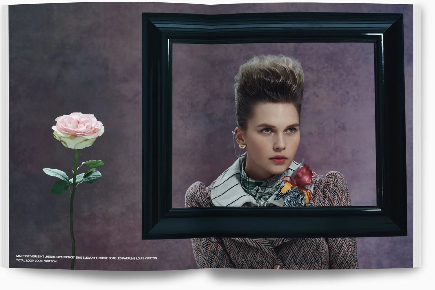 Ein junges Mädchen blickt durch einen schwarzen Bilderrahmen, daneben steht eine rosa Rose auf einem Stiel, im Hintergrund eine lilafarbene Wand.