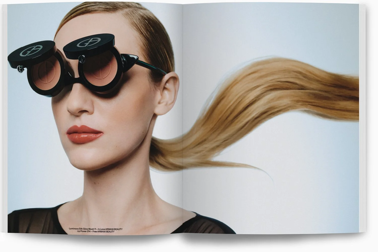 Eine Frau trägt große, dunkle Sonnenbrillen und hat lang, gewelltes blondes Haar, das sich im Wind bewegt.