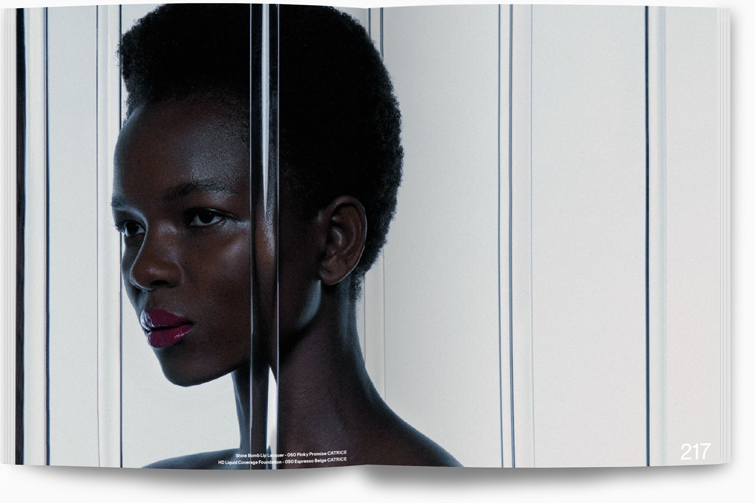 Porträt einer schwarzen Frau mit kurzen Haaren, deren Gesicht zur Seite gedreht ist, vor einer silbernen, vertikalen metalischen Wand. Sie trägt leichten Make-up mit rotem Lippenstift.