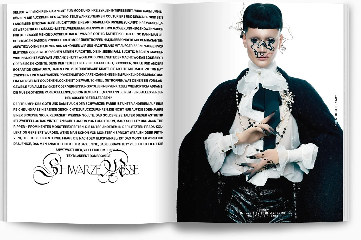 Modisch gekleidete Person mit schwarzem Bob, kunstvollem Make-up und schwarzer Nagellack, trägt elegante Kleidung mit Perlenkette und Brosche, vor grauem Hintergrund.