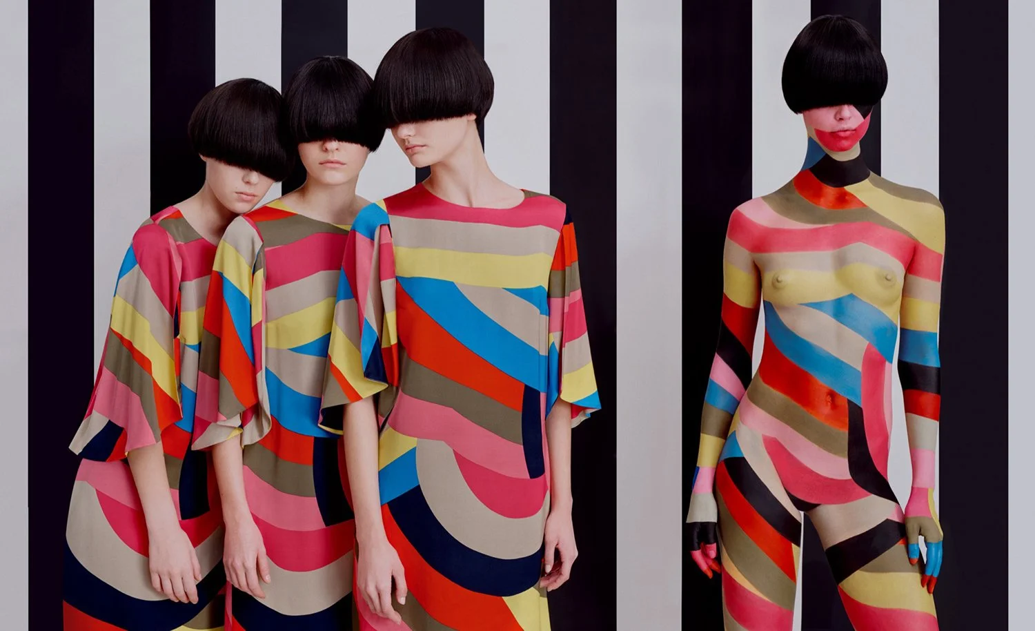 Four models in colorful, striped, abstract-patterned dresses with black bob hairstyles, standing in front of a black and white striped background. One model on the far right is topless, with the dress painted on her body.