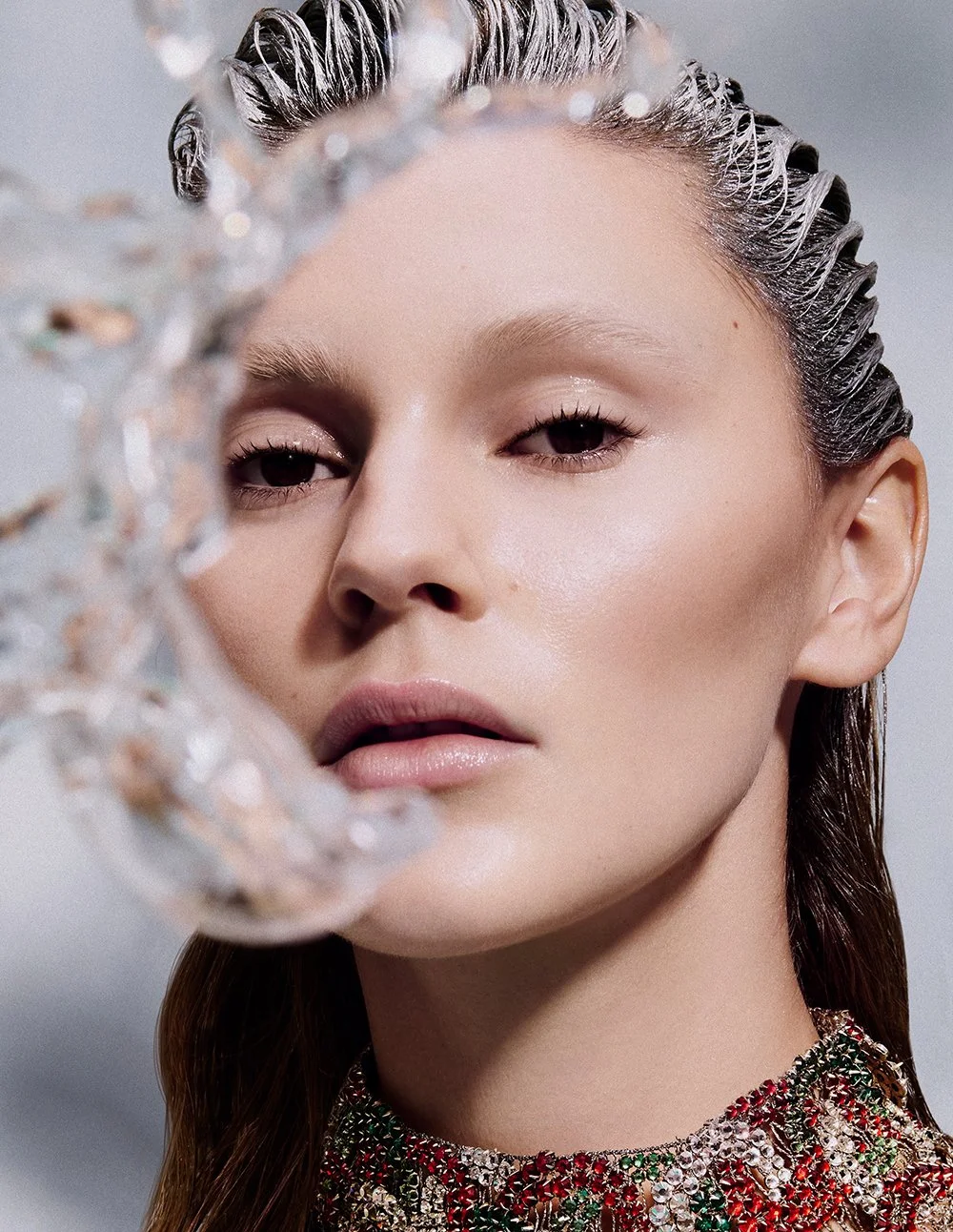 Nahaufnahme eines Models mit nassem, glänzendem Haar, das mit Wasser bespritzt ist, vor neutralem Hintergrund.