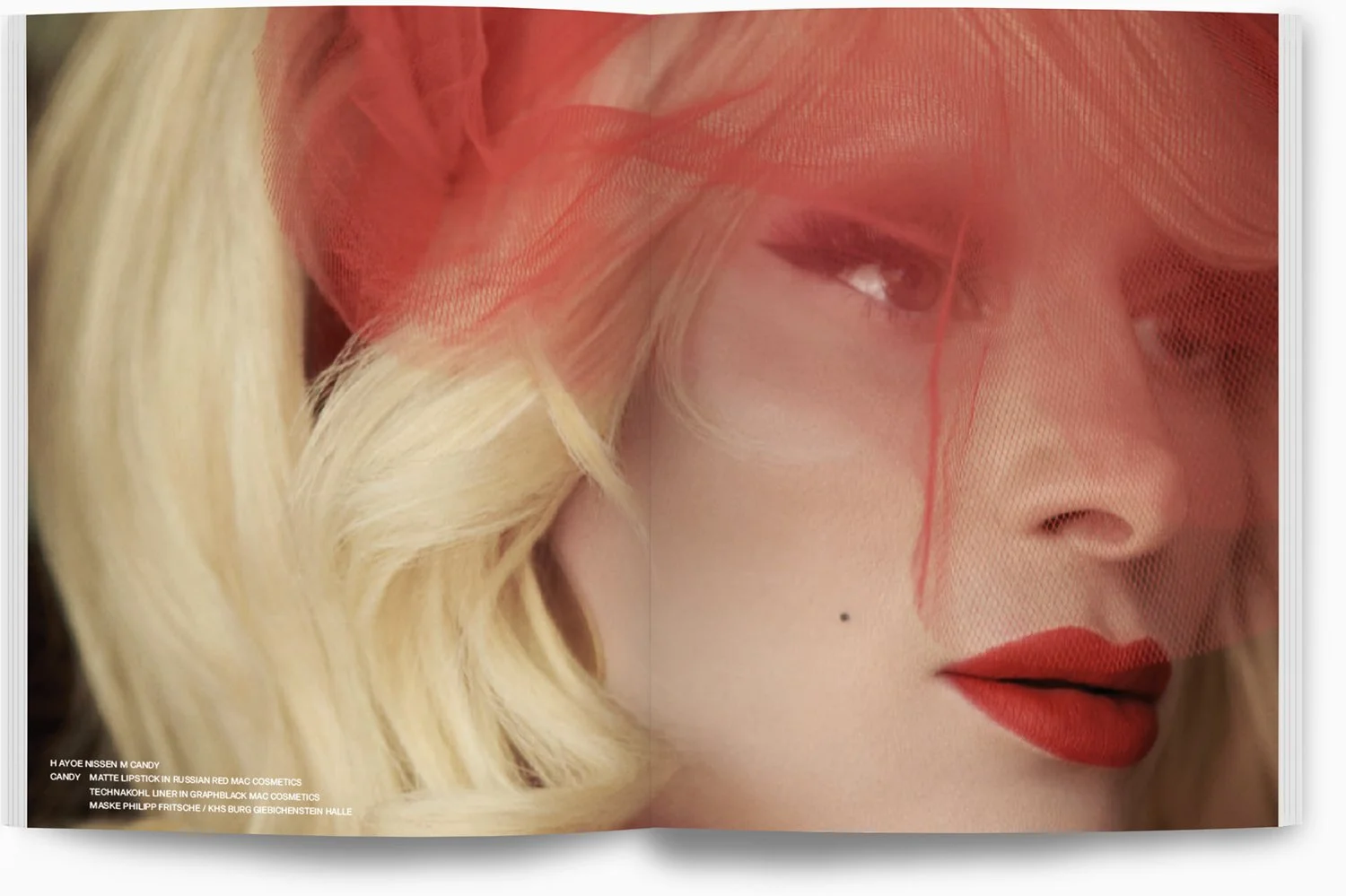 Nahaufnahme eines Gesichts einer Frau mit blonden Locken, rotem Lippenstift und rotem Netz, das ihr Gesicht teilweise verdeckt.