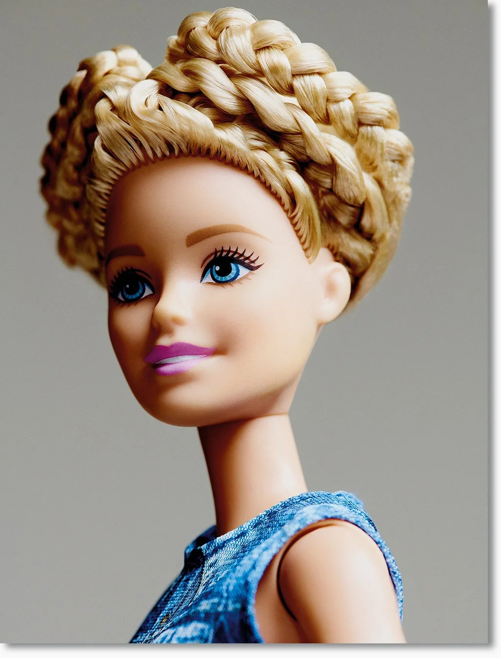 Puppenkopf mit blond gewellten Haaren, blauen Augen und pinken Lippen, trägt ein blaues Oberteil.