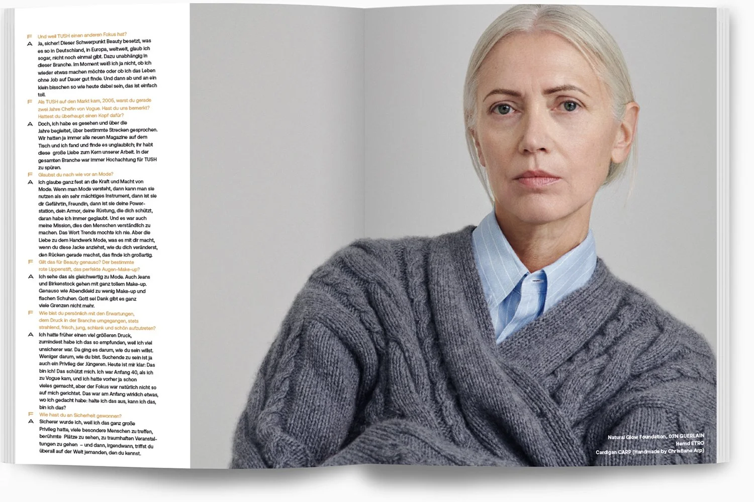 Nahaufnahme einer älteren Frau mit blondem Haar, die eine graue Strickjacke und eine blaue Hemdbluse trägt, vor einem neutralgrauen Hintergrund.