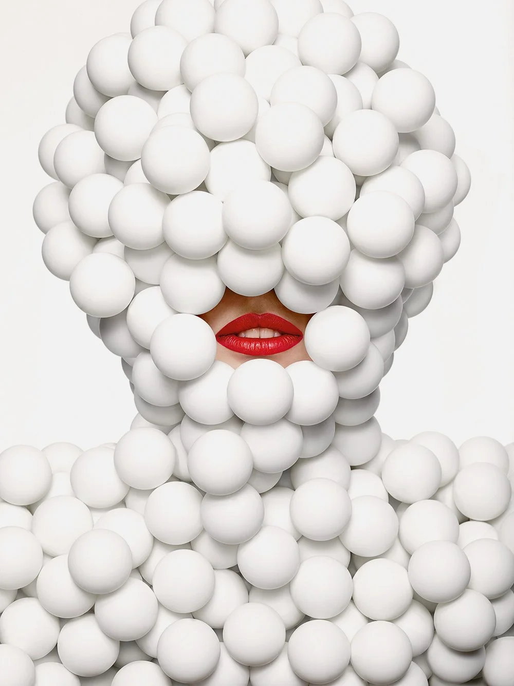 Person mit roten Lippen, kaum sichtbar durch eine Maske aus weißen Kugeln.